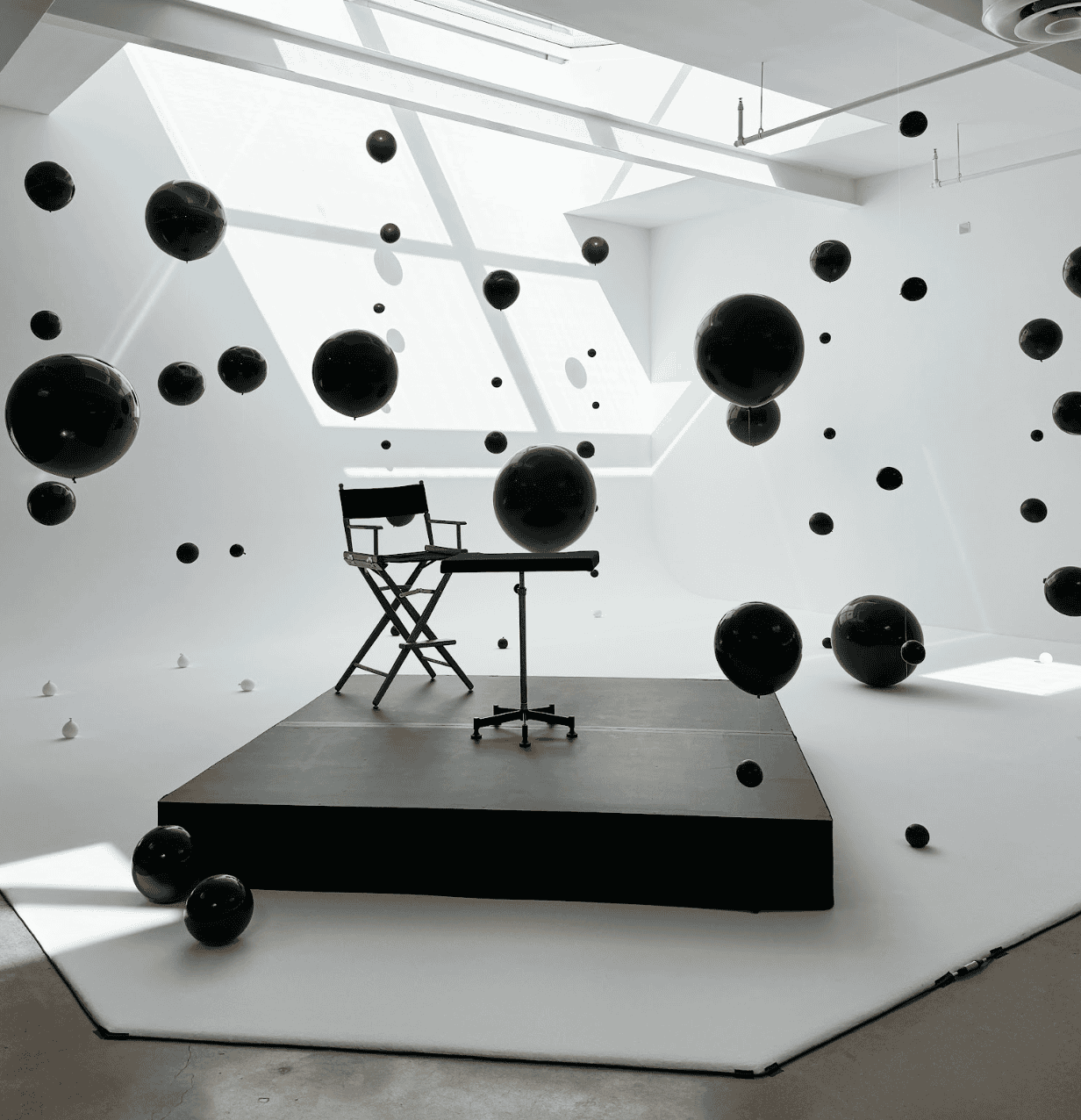 Black and white studio space with floating black balloon spheres around a director's chair