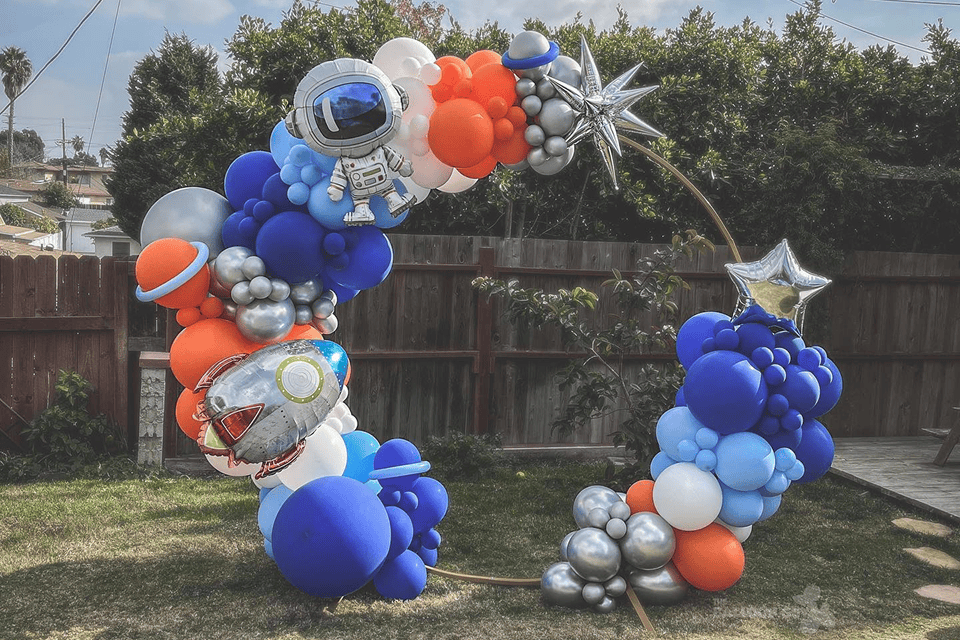 Space-themed circular balloon garland with astronaut, rocket and planet foil balloons in a backyard