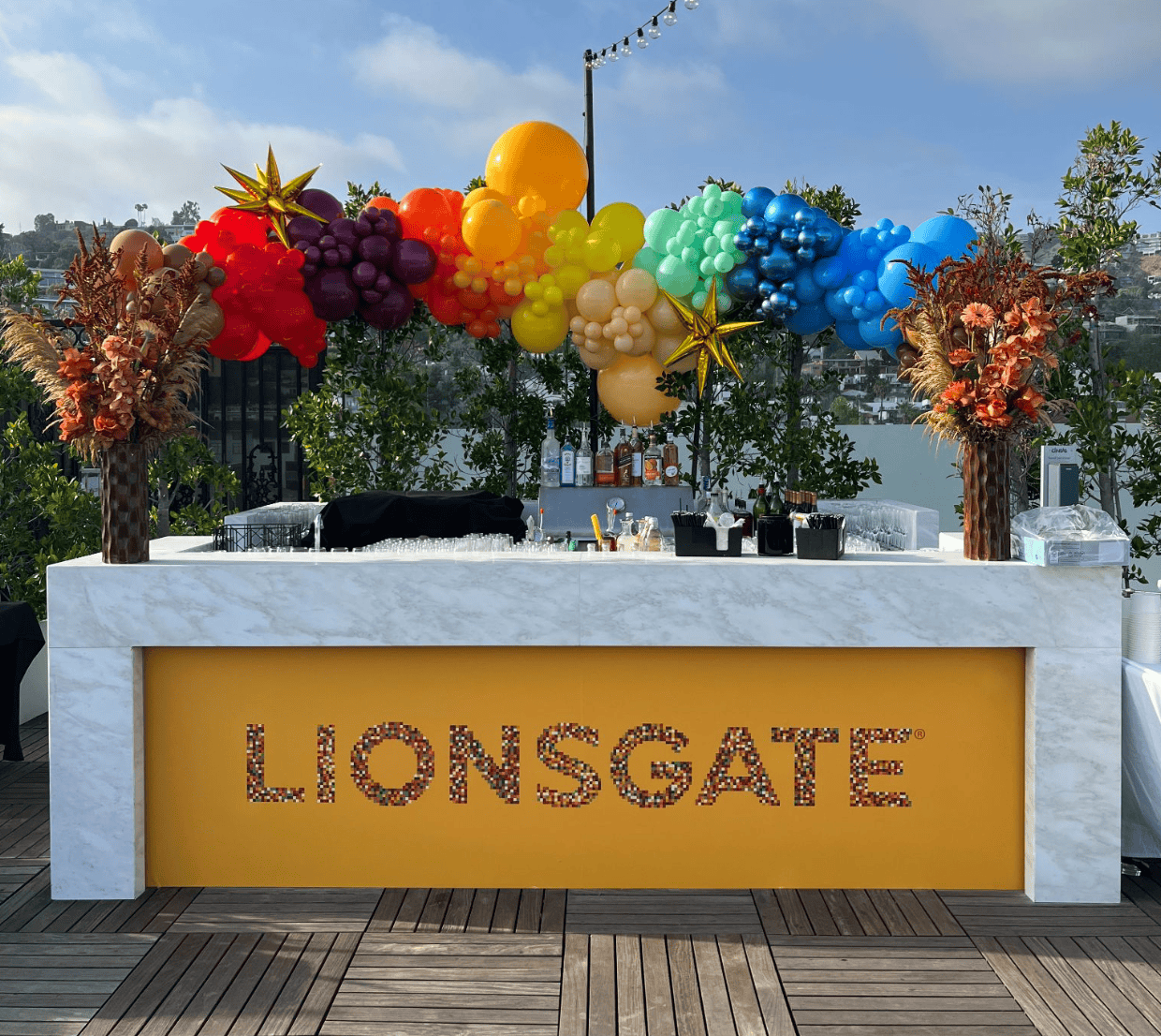 Rooftop bar with Lionsgate-branded counter and a rainbow balloon garland arch above