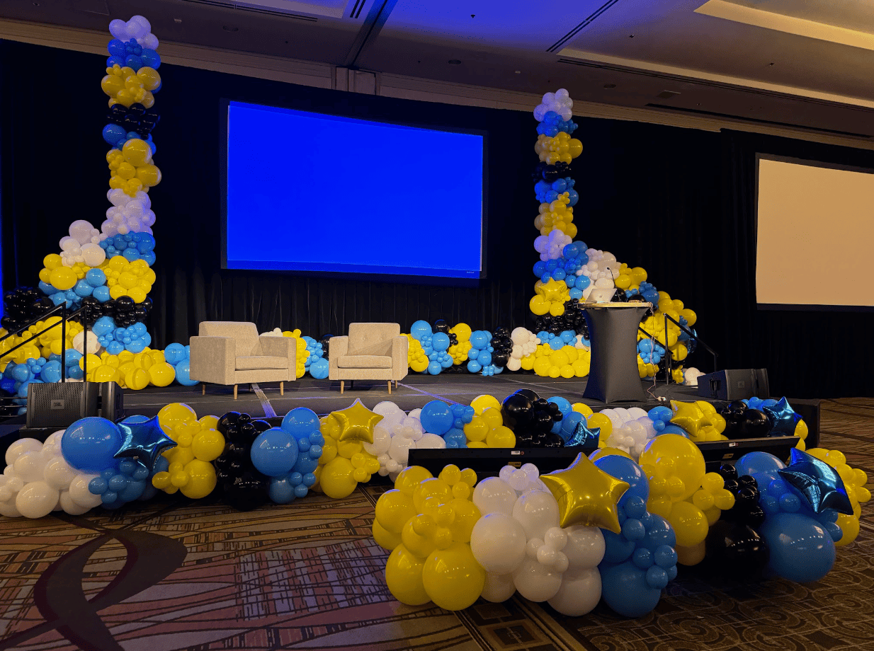 Conference stage decorated with blue, yellow, black and white balloon columns