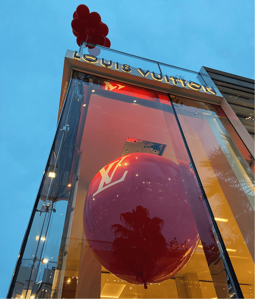 Louis Vuitton storefront at dusk with a giant branded red balloon sphere in the window display