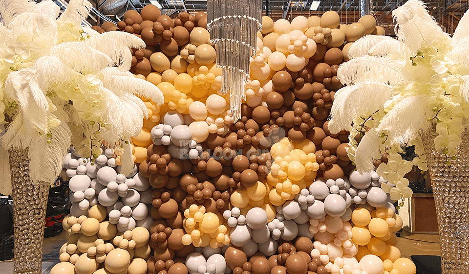 Earth-toned brown, tan and cream balloon wall between feather arrangements under a chandelier