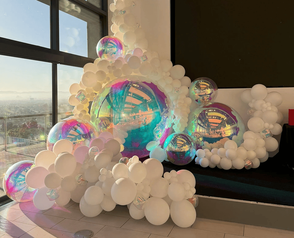 White balloon cloud with large iridescent mirror spheres beside a high-rise window