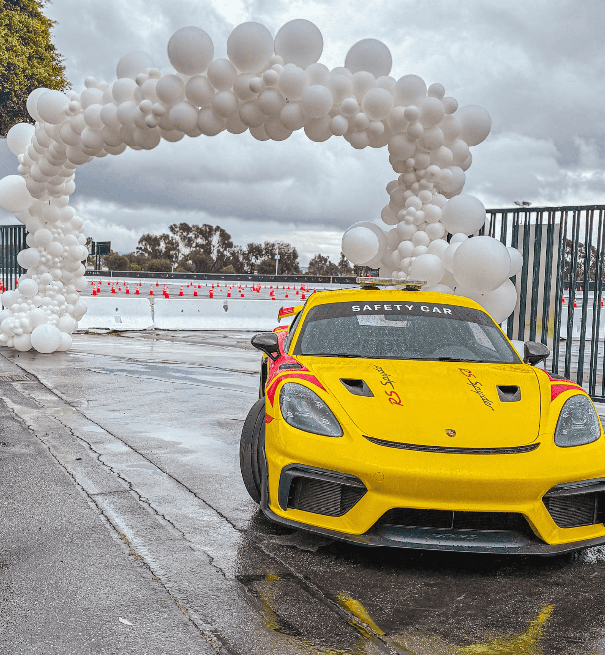 Yellow Porsche safety car under a white organic balloon arch at a racing event