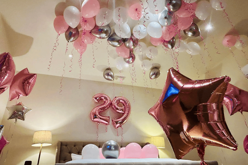 Hotel room ceiling filled with pink, white and silver balloons and a number 29 foil balloon