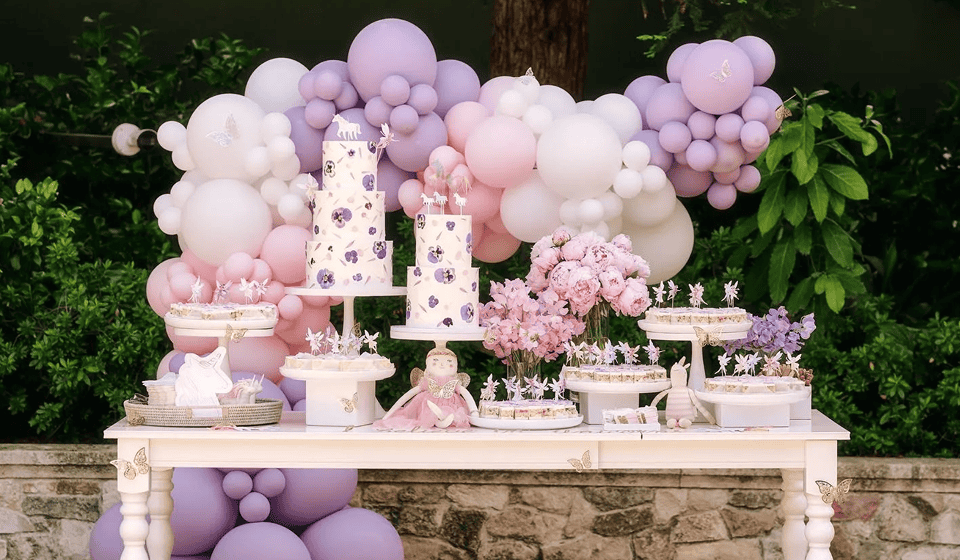 Lavender and pink balloon garland behind a dessert table with tiered cakes