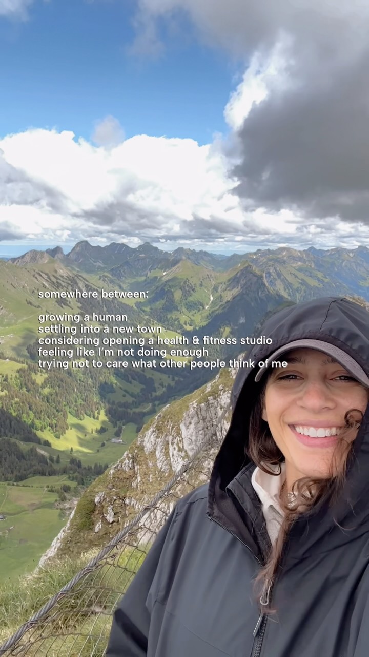 Chloe smiling in a rain jacket on a mountain summit above an alpine valley