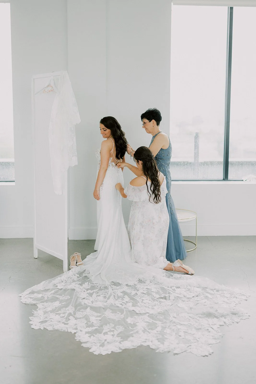 Bride being helped into her wedding gown by two women in a bright minimalist bridal suite