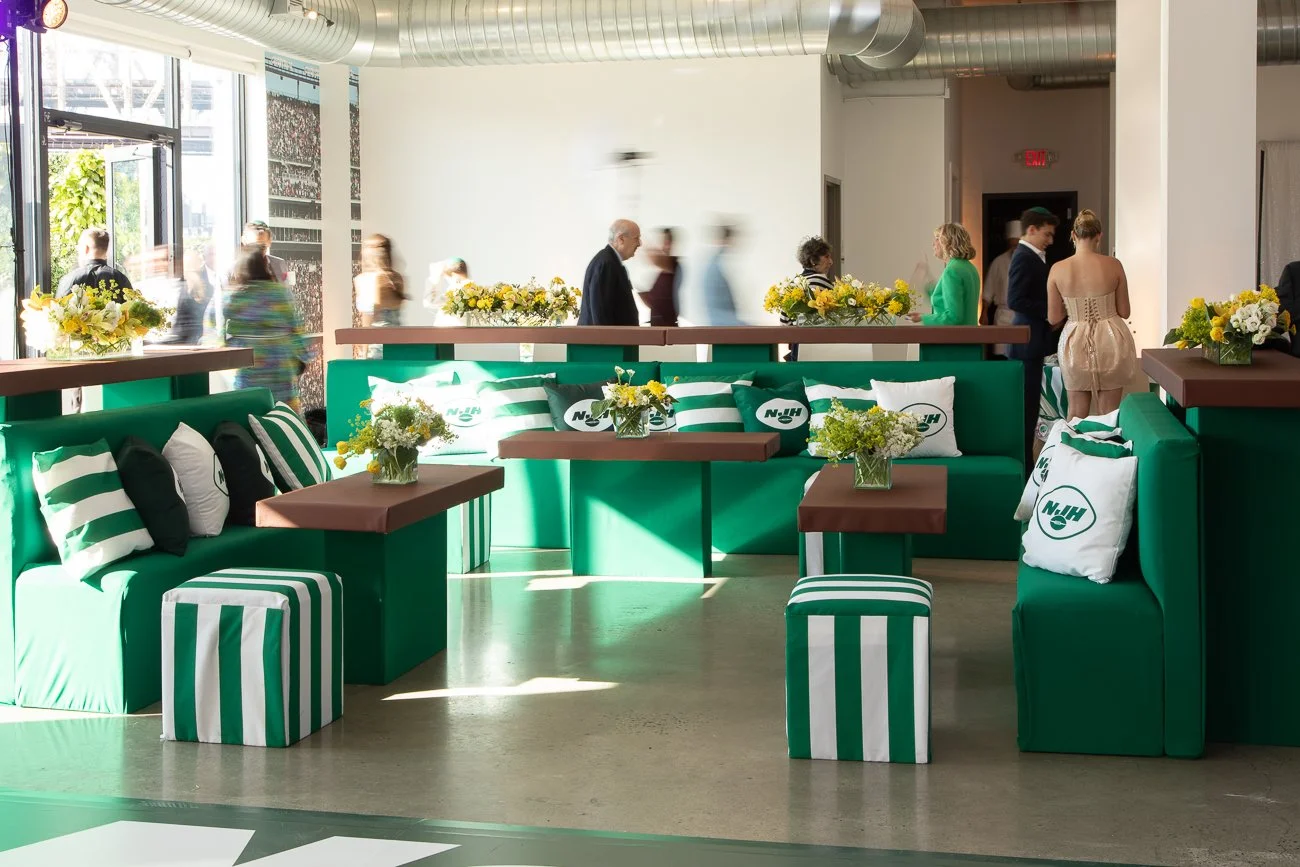 Indoor event space decorated for a NY Jets themed party with green banquette seating and striped ottomans