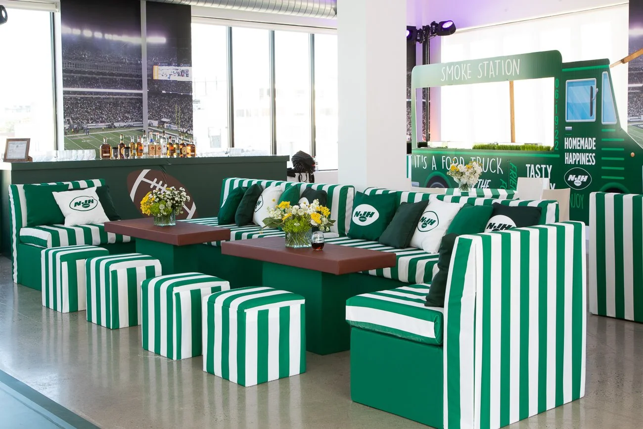 Indoor event space set for a NY Jets themed event with striped furniture, branded food truck prop and bar