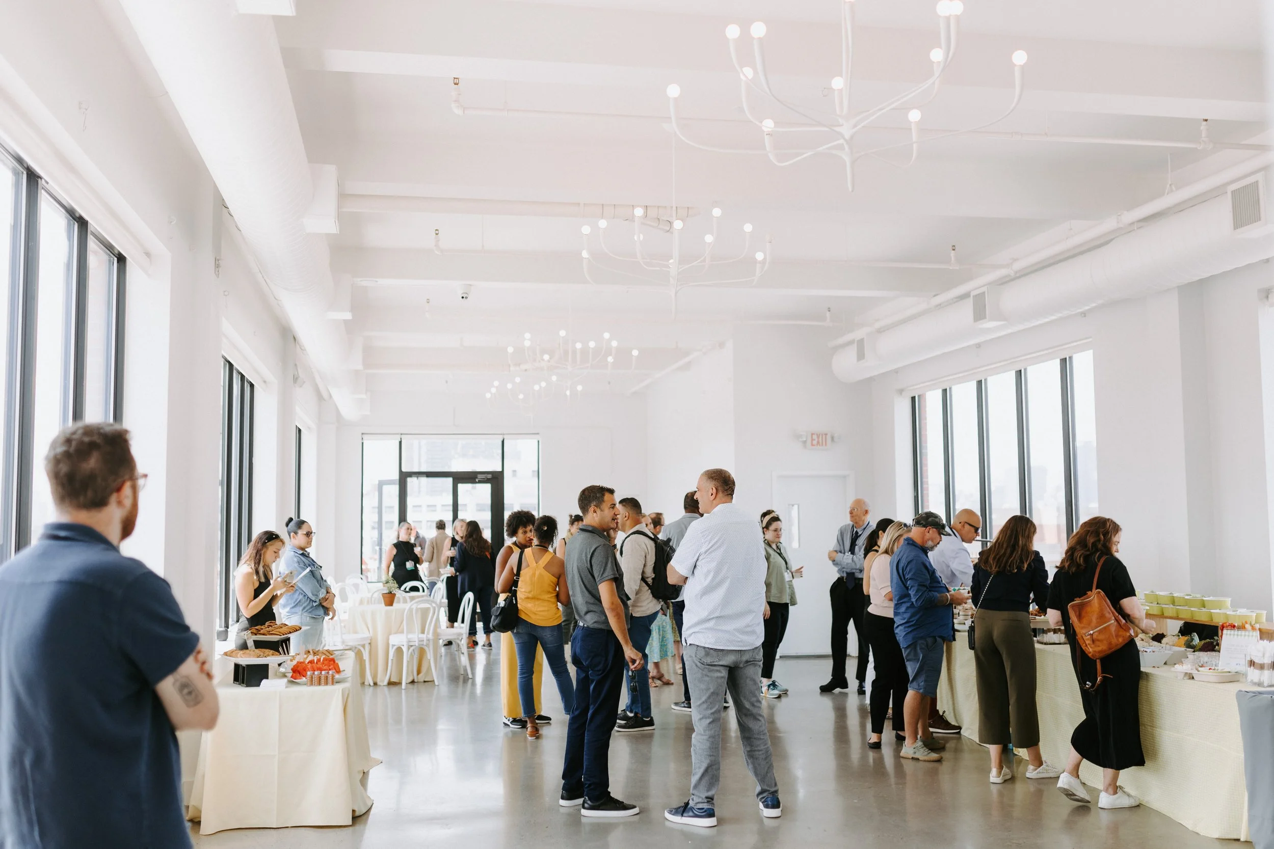 Crowd of attendees mingling at a catered corporate event in a bright white event space
