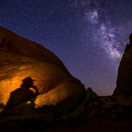 Silhouette of a person sitting against glowing rock formations under the Milky Way