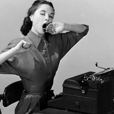 Vintage black-and-white photo of a woman yawning at a typewriter