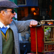 An older man yawning or calling out while holding a birdcage with a parrot