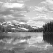 Black-and-white photograph of a calm mountain lake with a forested shoreline
