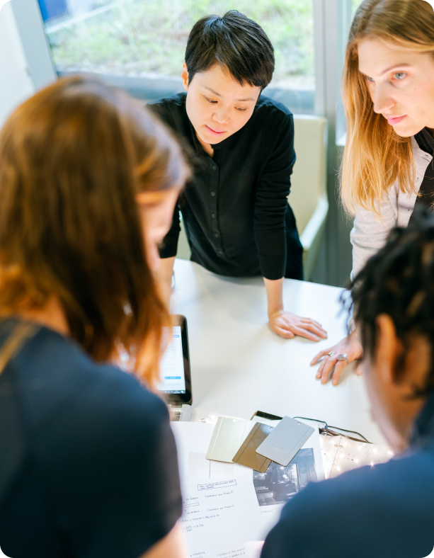 A small group of diverse colleagues leaning over a white table, reviewing documents together