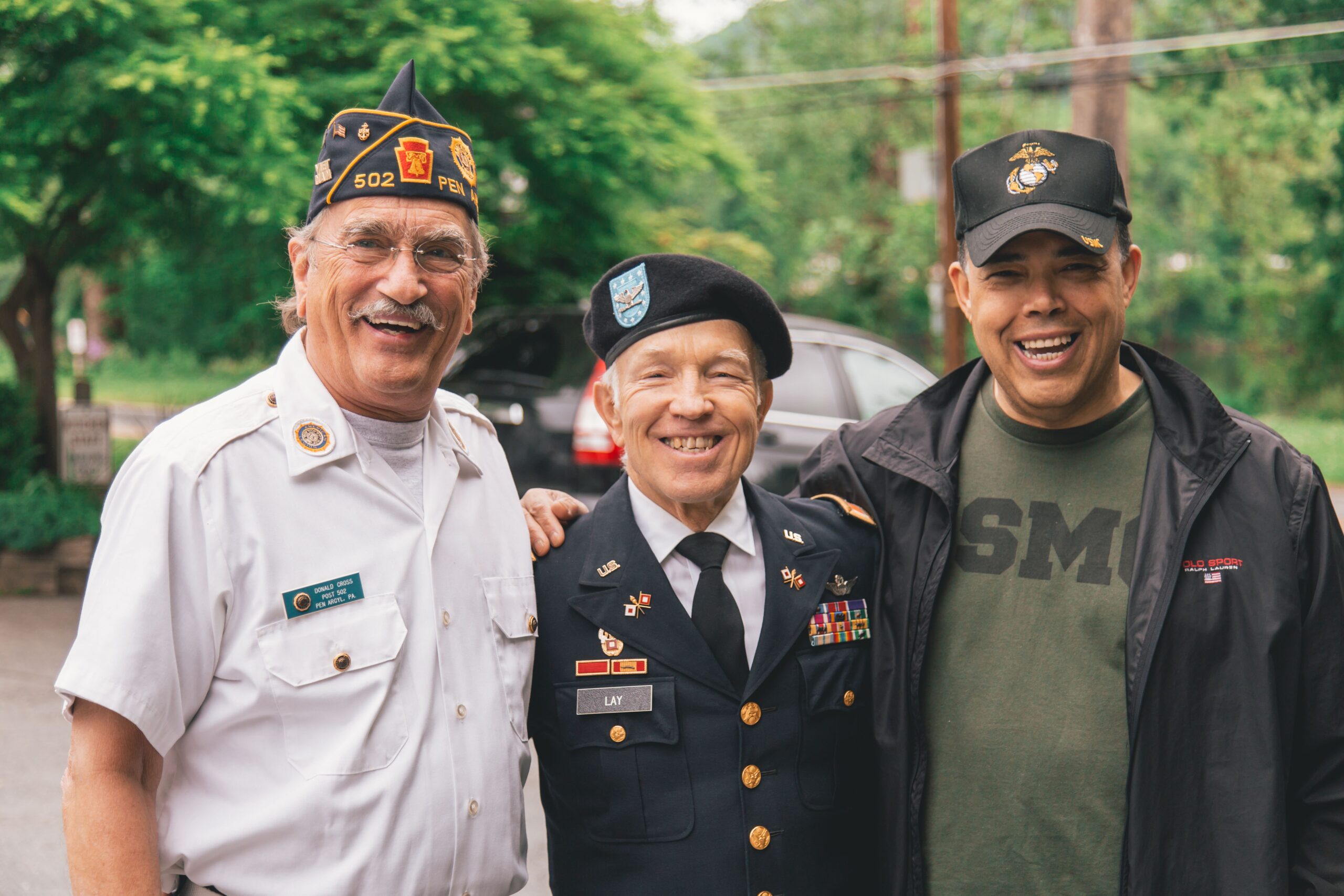 Three smiling military veterans in uniform and caps standing together outdoors