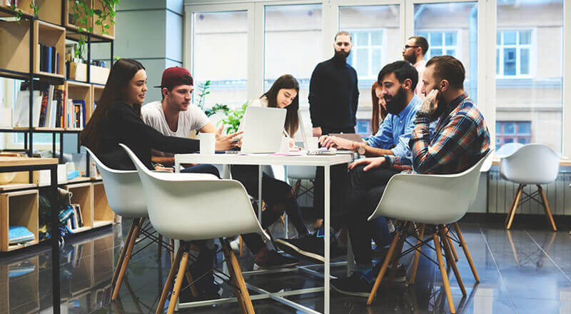 Young professionals gathered around a round table in a modern open office, working on laptops