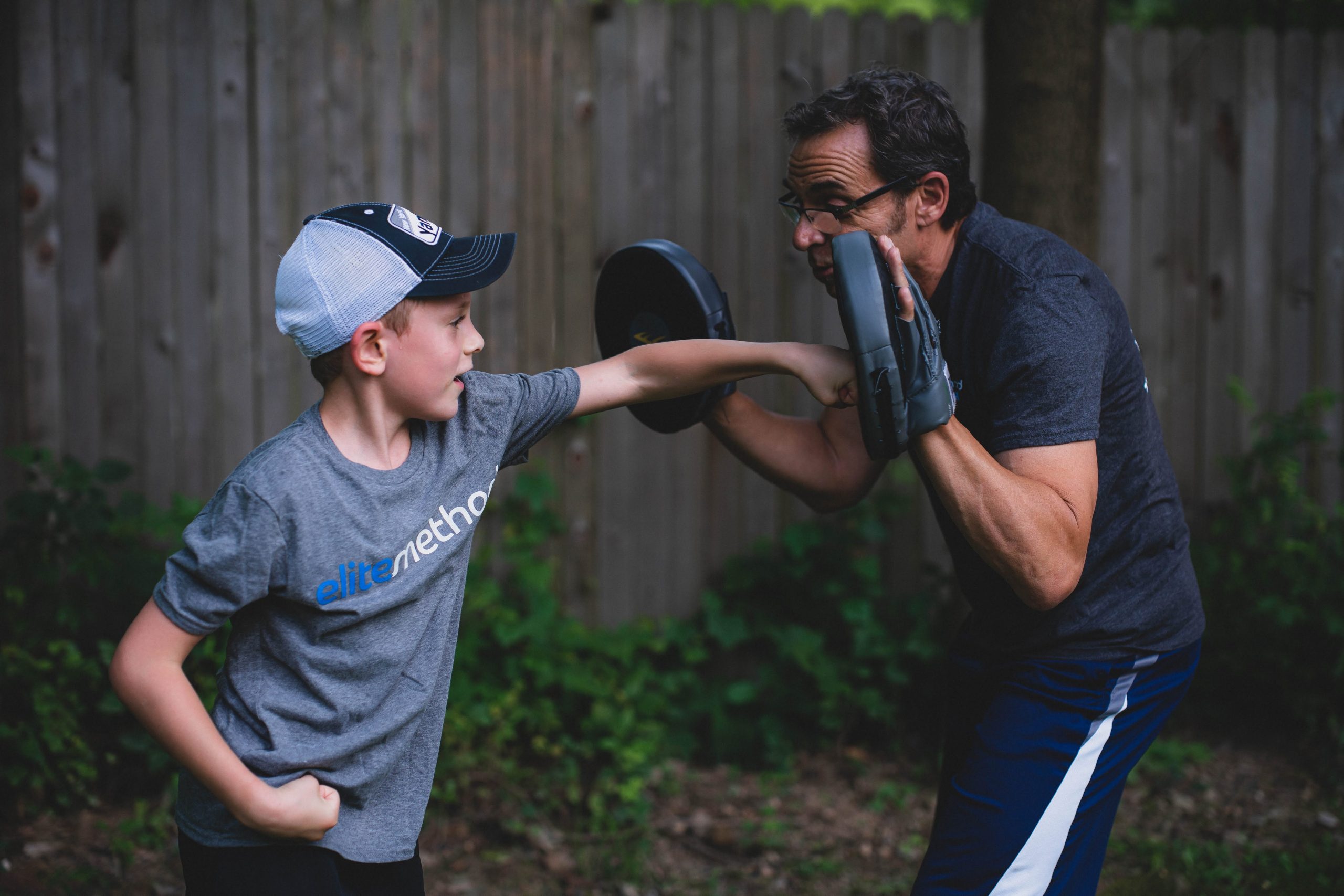 Child in an Elite Method shirt punching a pad held by a coach in a backyard