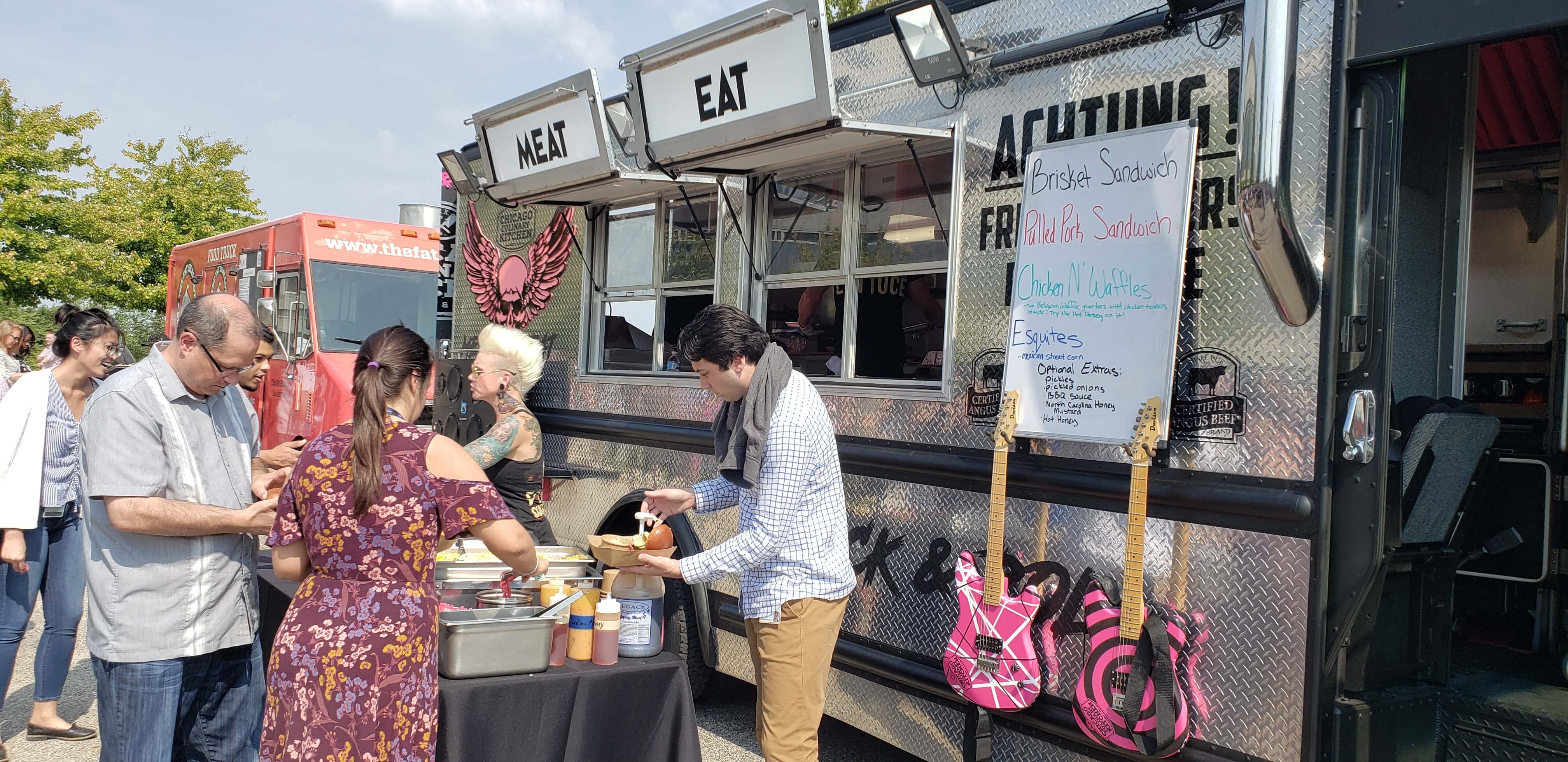 Customers ordering at a dark metallic food truck with pink electric guitars on display