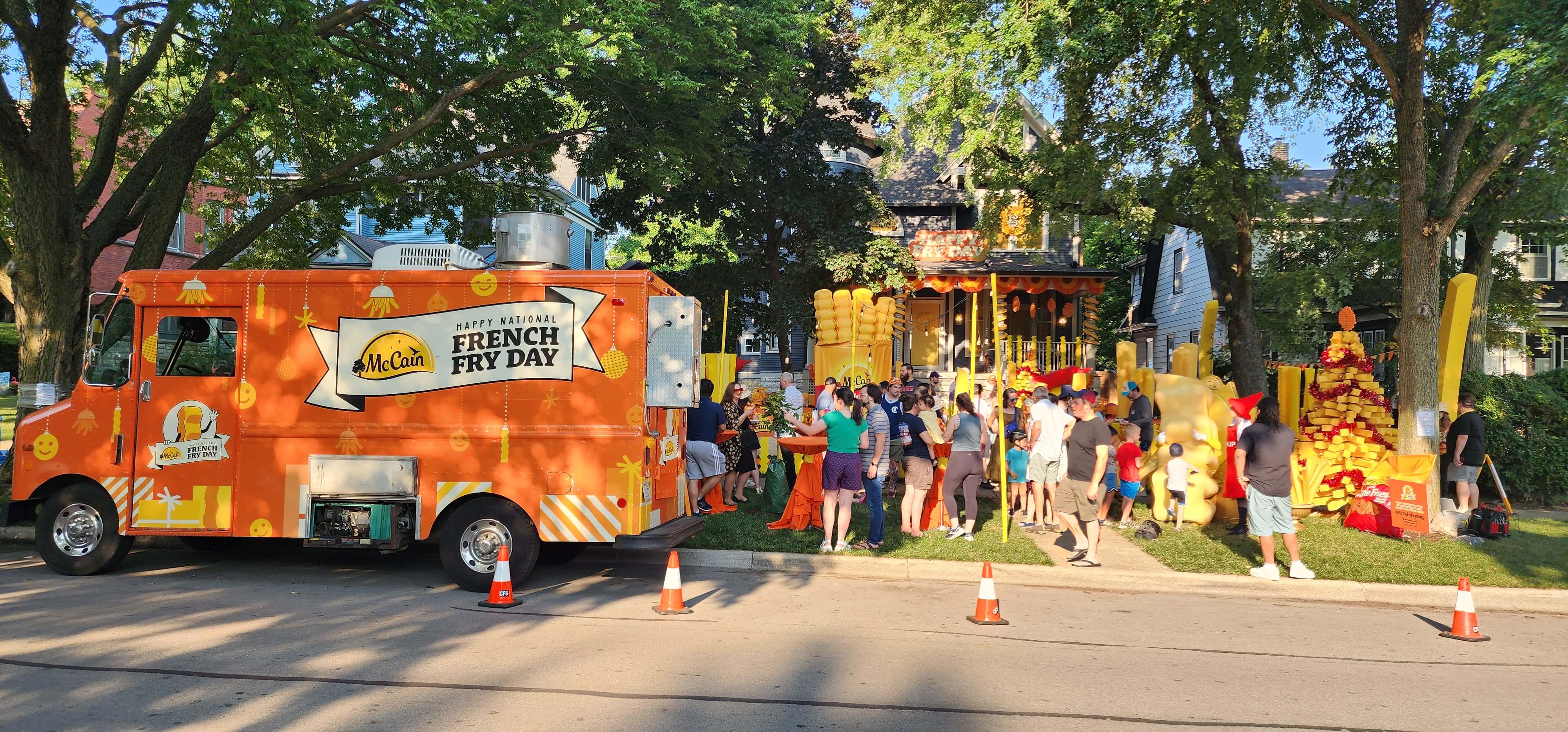 McCain French Fry Day branded orange food truck with a festive crowd on a residential street