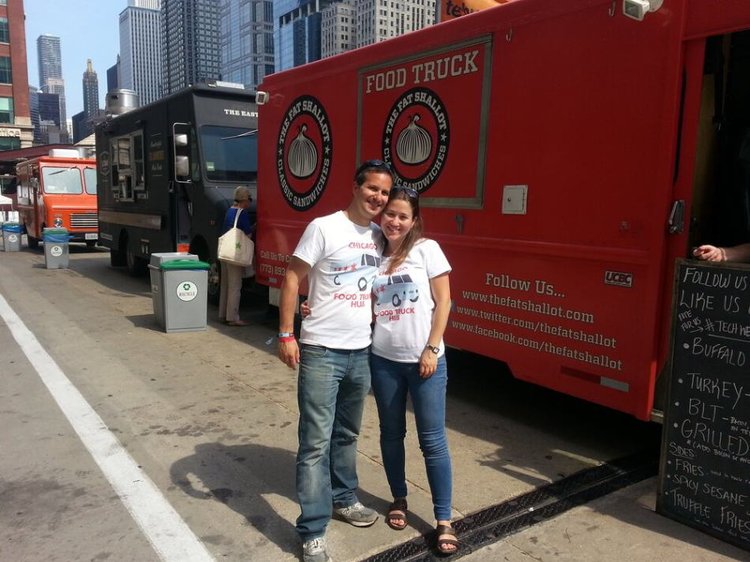 Man and woman in Food Truck Hub branded T-shirts posing in front of the red Fat Shallot food truck