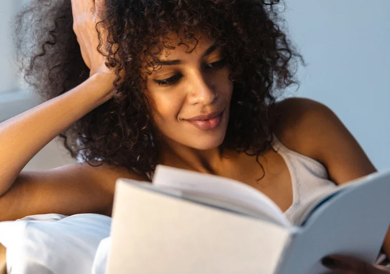 A woman relaxing in bed, reading and smiling at The Rest Spot