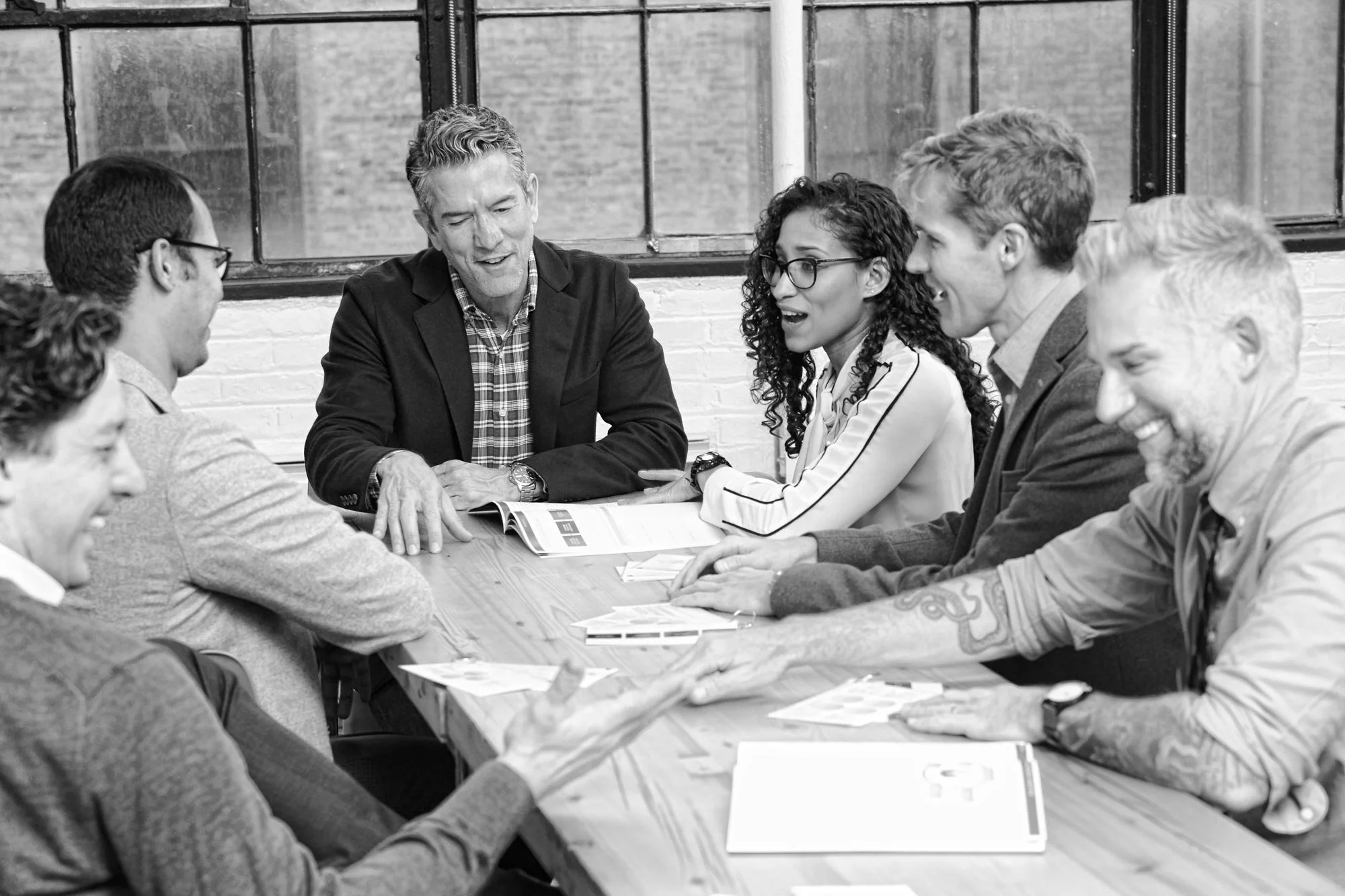 Six professionals in animated discussion around a wooden table in an industrial loft