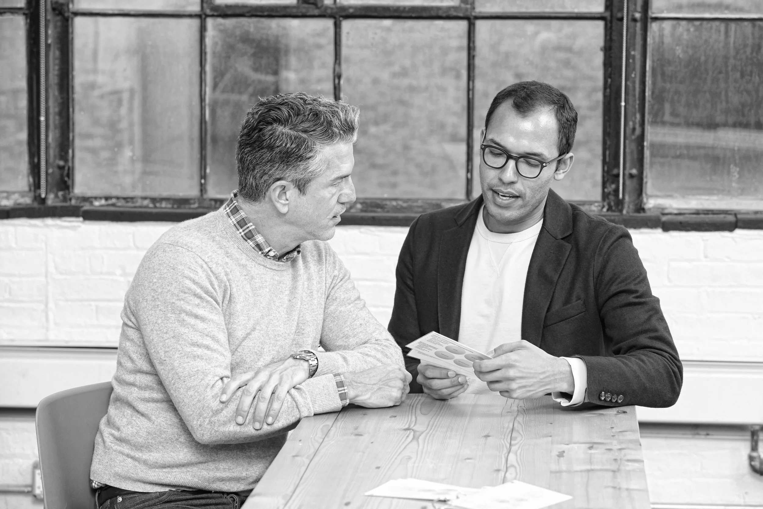 Two men reviewing printed materials at a wooden table in an industrial loft