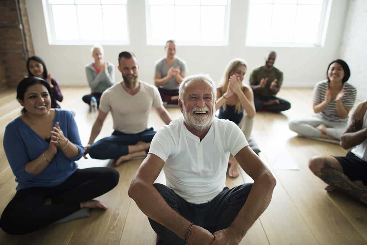 Large diverse group seated cross-legged on a studio floor with a smiling wellness instructor