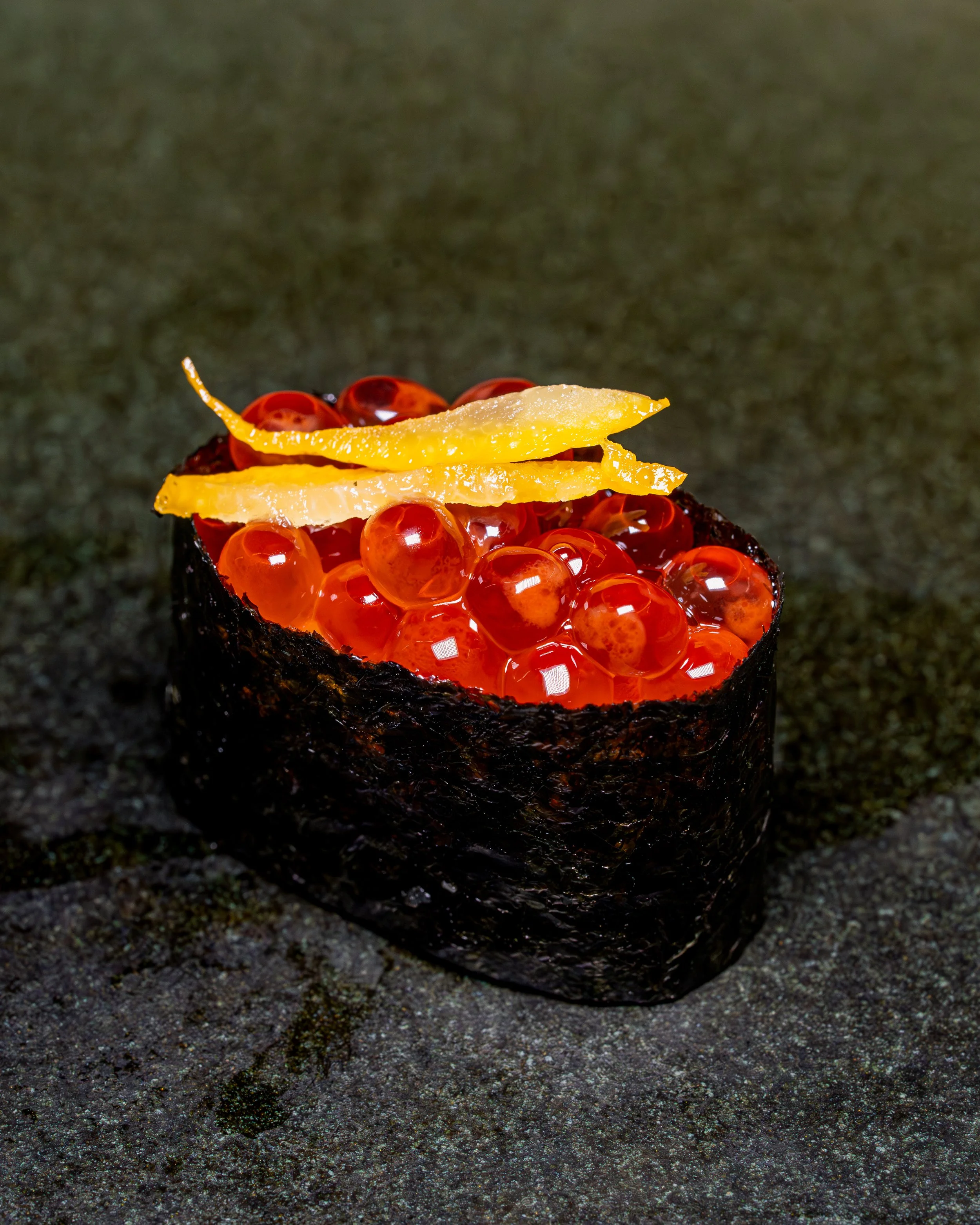 Ikura gunkan sushi topped with strips of yuzu zest on dark stone