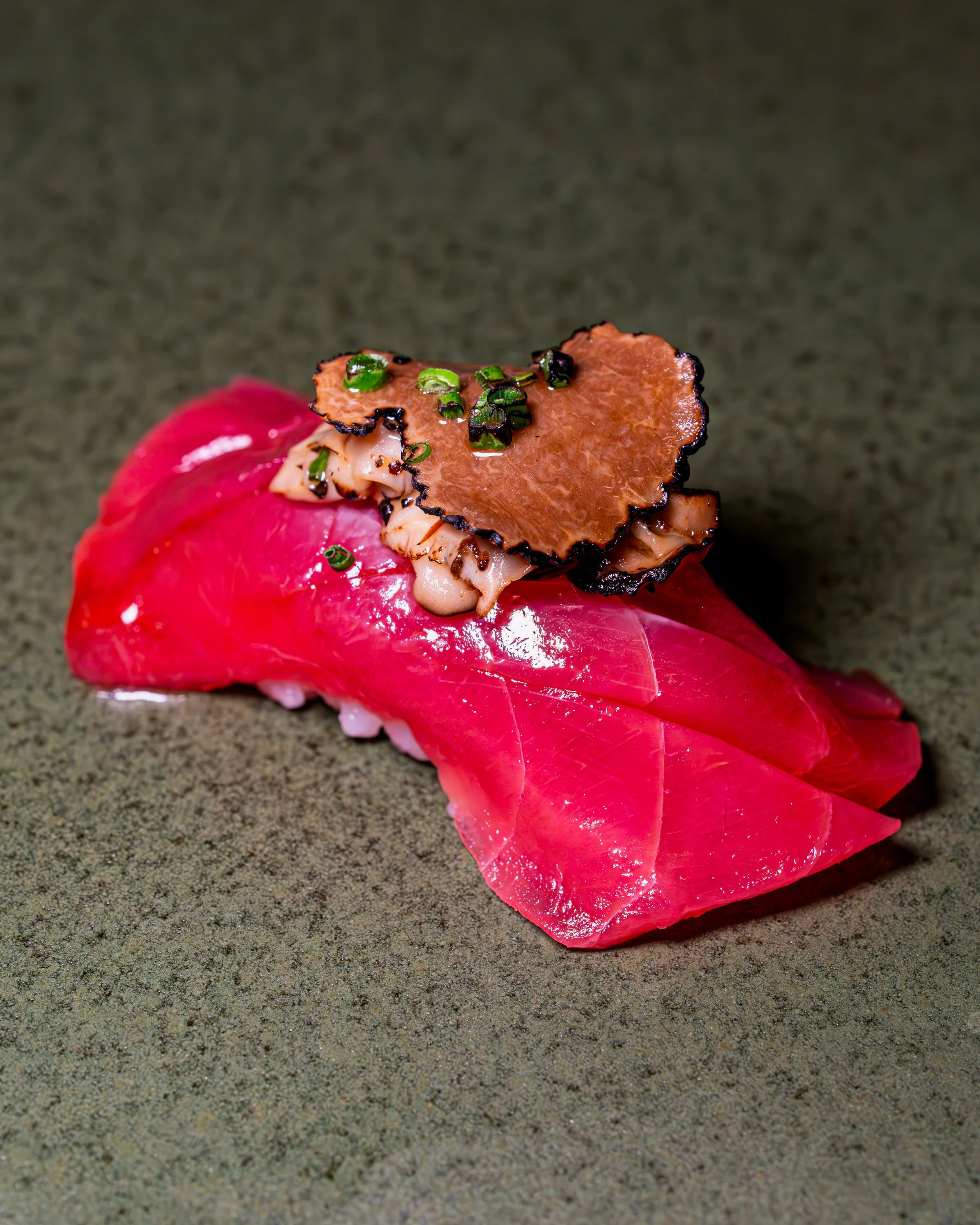 Tuna nigiri topped with shiitake mushroom and a truffle slice on speckled grey stone