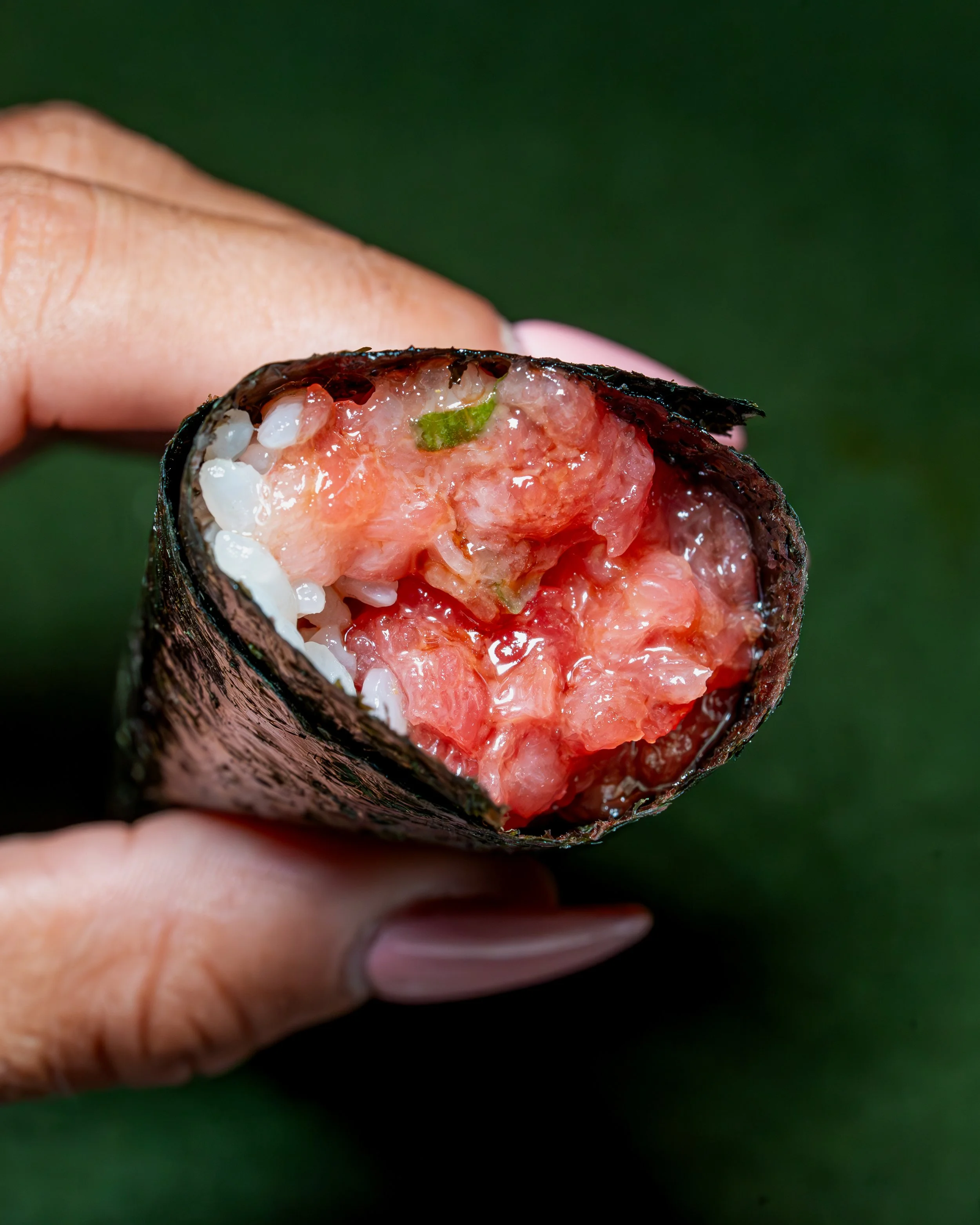 Toro hand roll held in hand with the cross-section visible against a deep green background