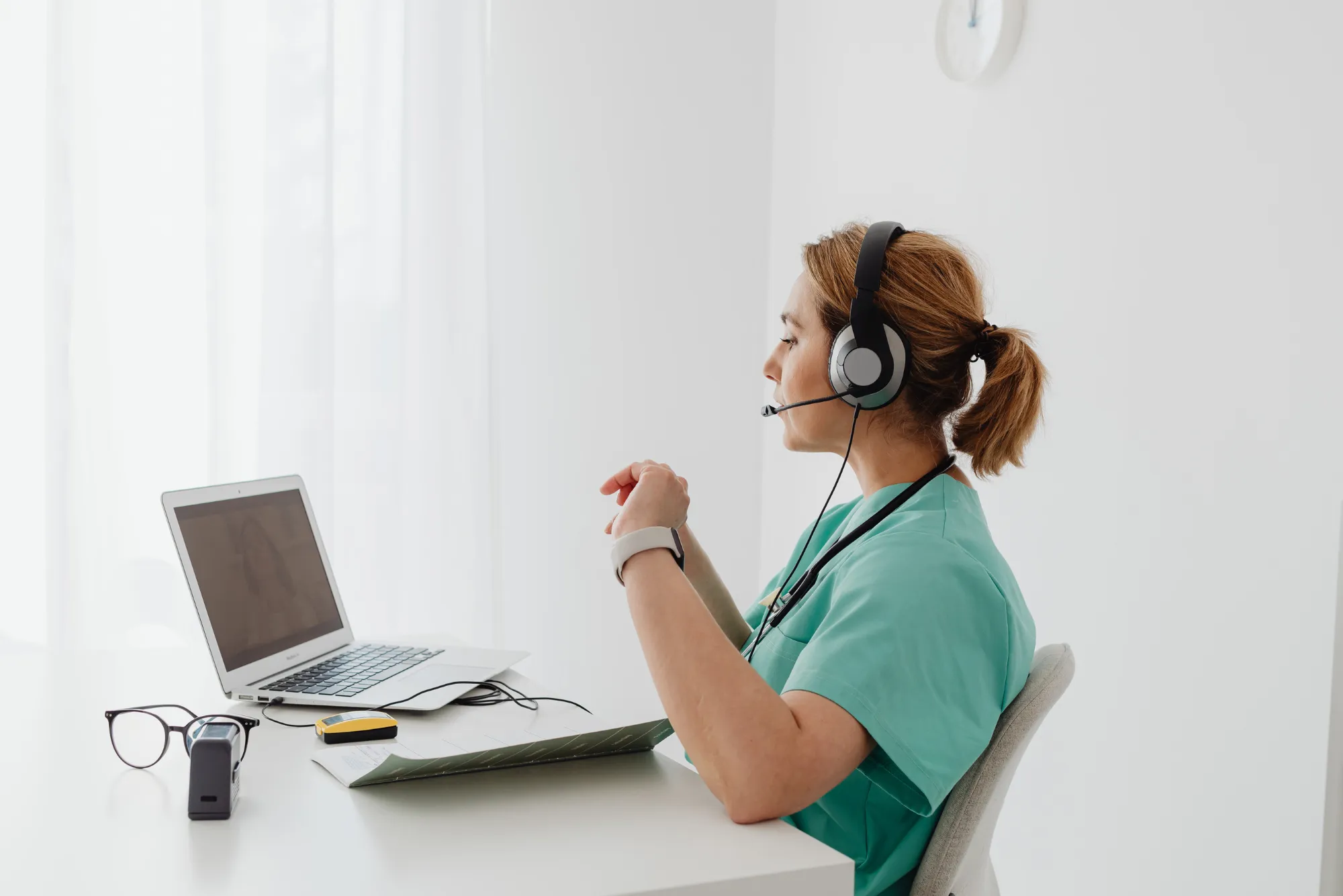 Female clinician in scrubs with a headset working at a laptop