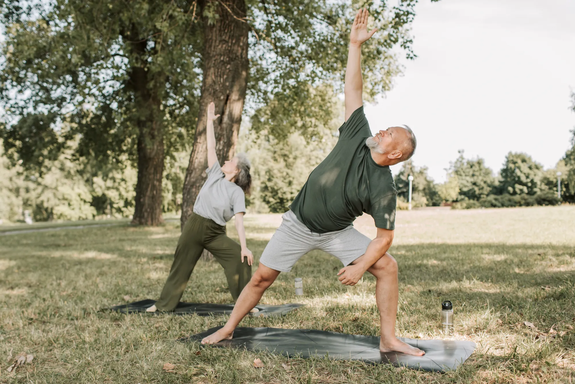 Older couple doing yoga and stretching outdoors in a park
