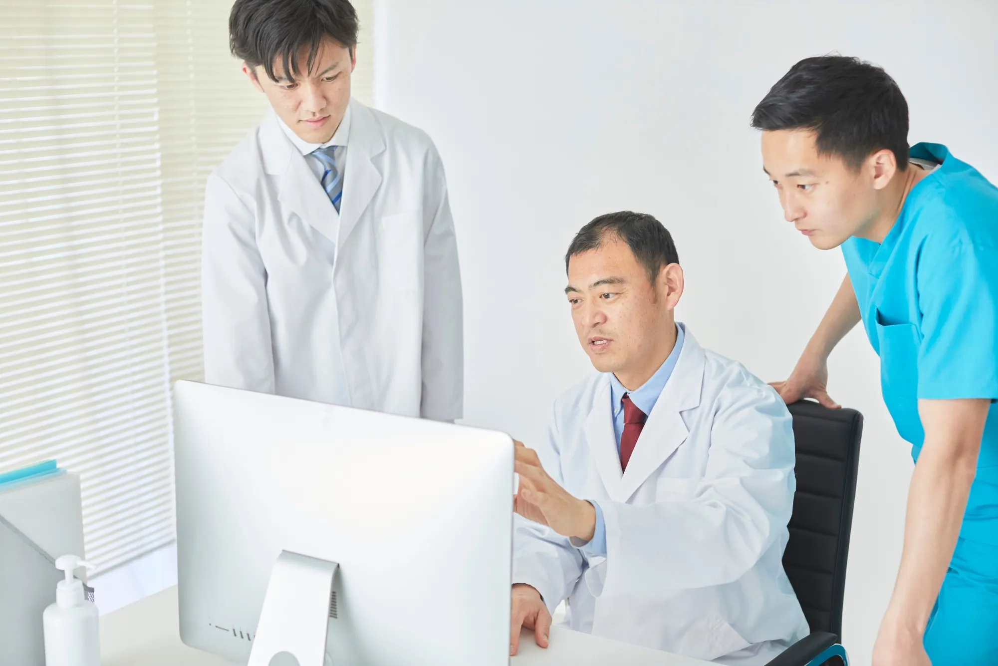 Three medical professionals in lab coats reviewing data on a desktop computer