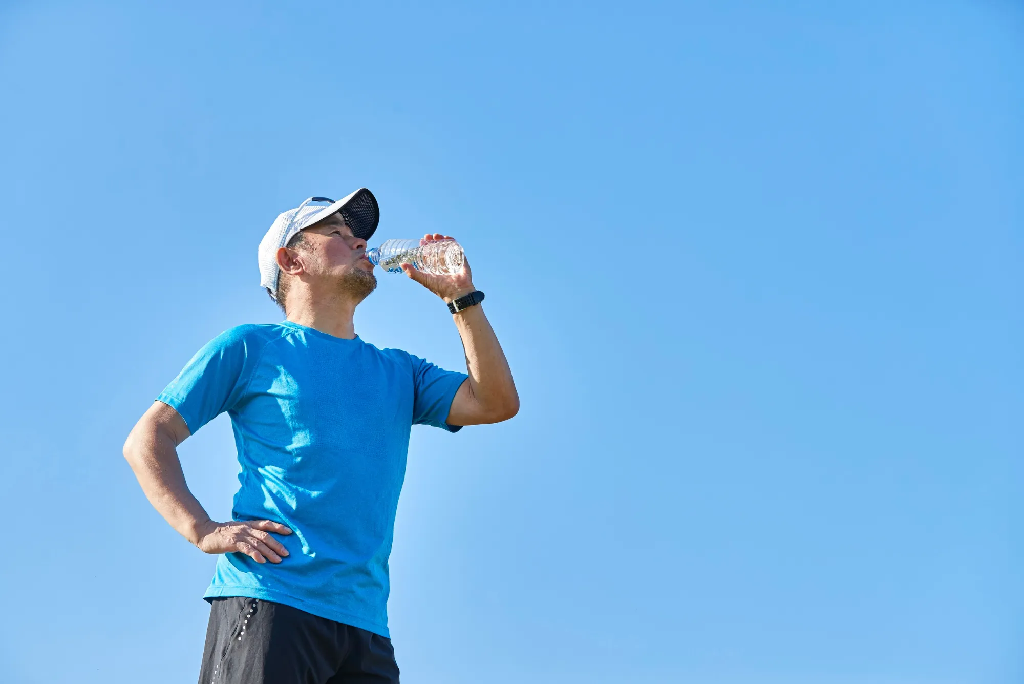 Male runner drinking water against a blue sky