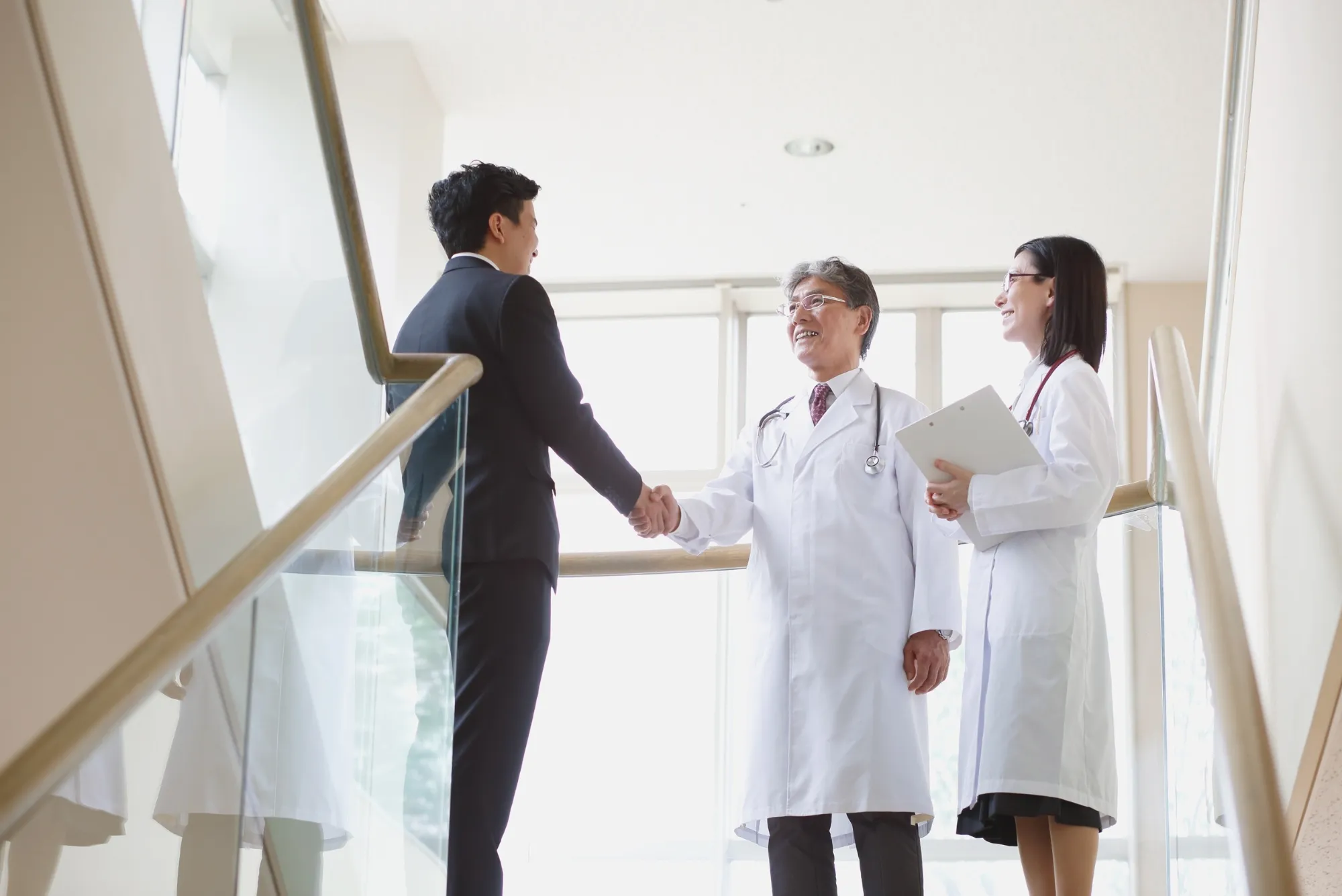 Business executive shaking hands with a senior doctor in a hospital corridor