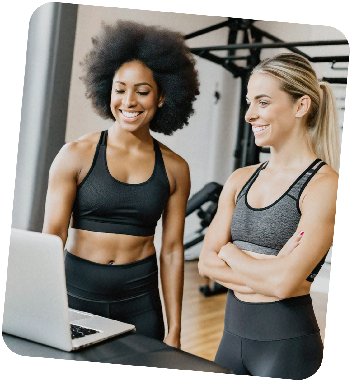 Two women in sportswear smiling at a laptop in a gym