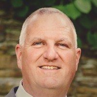 Bill McDevitt, business coach, smiling in front of a stone wall