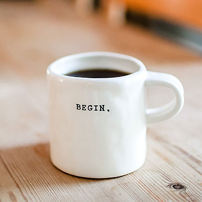A white mug reading BEGIN on a wooden surface