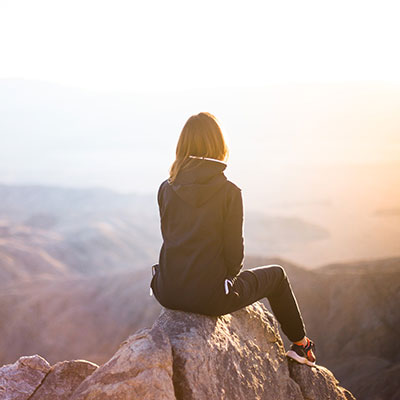 A person sitting on a rock over misty mountain peaks at sunrise