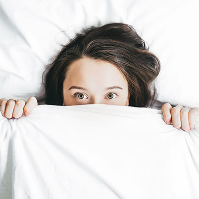 A woman peeking over white bed covers