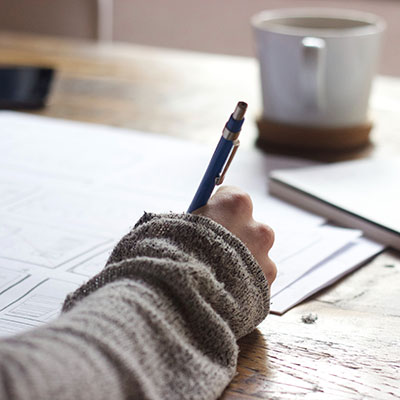 A hand writing on paper with coffee nearby