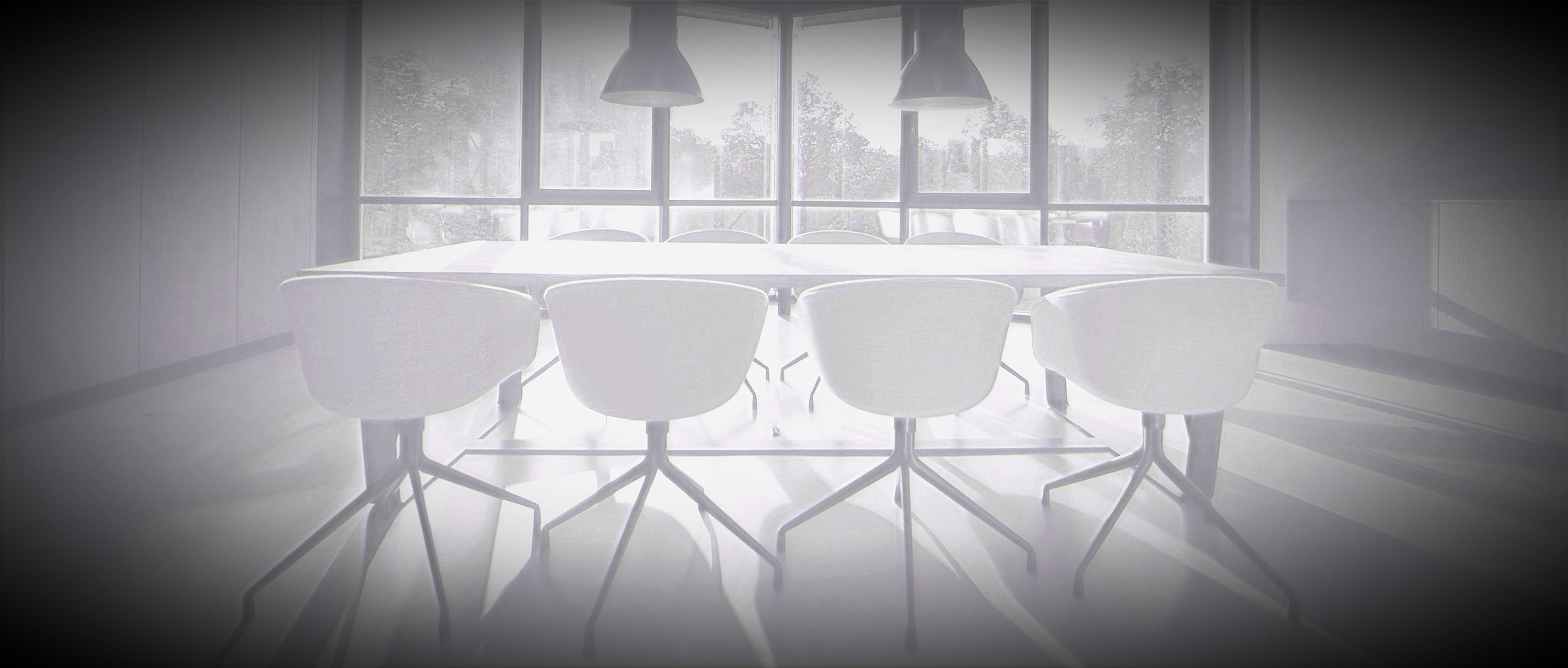 Luminous high-key black and white modern conference room with a white table, white chairs, pendant lights and large windows overlooking trees.