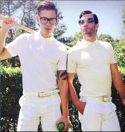 Two men in all-white outfits holding croquet mallets in bright sunlight