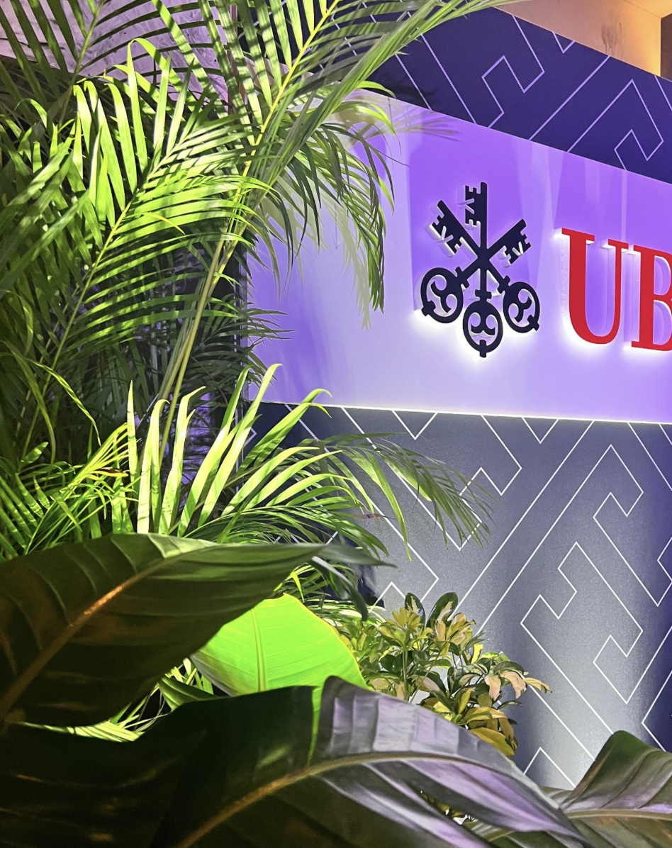 Illuminated UBS branded event wall framed by lush tropical greenery