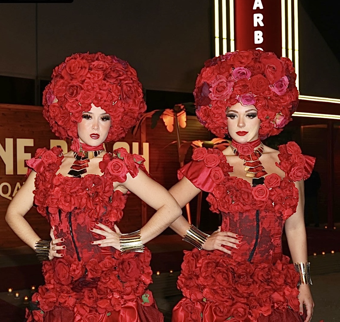 Two performers in elaborate red rose gowns and headdresses