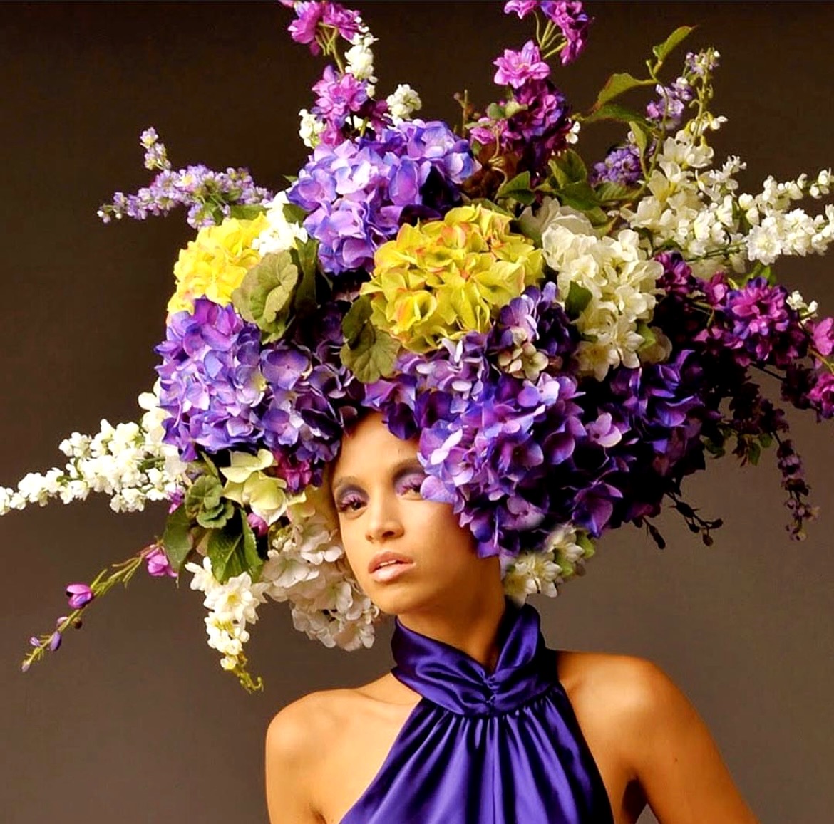 Model wearing a dramatic floral headdress with a purple satin halter
