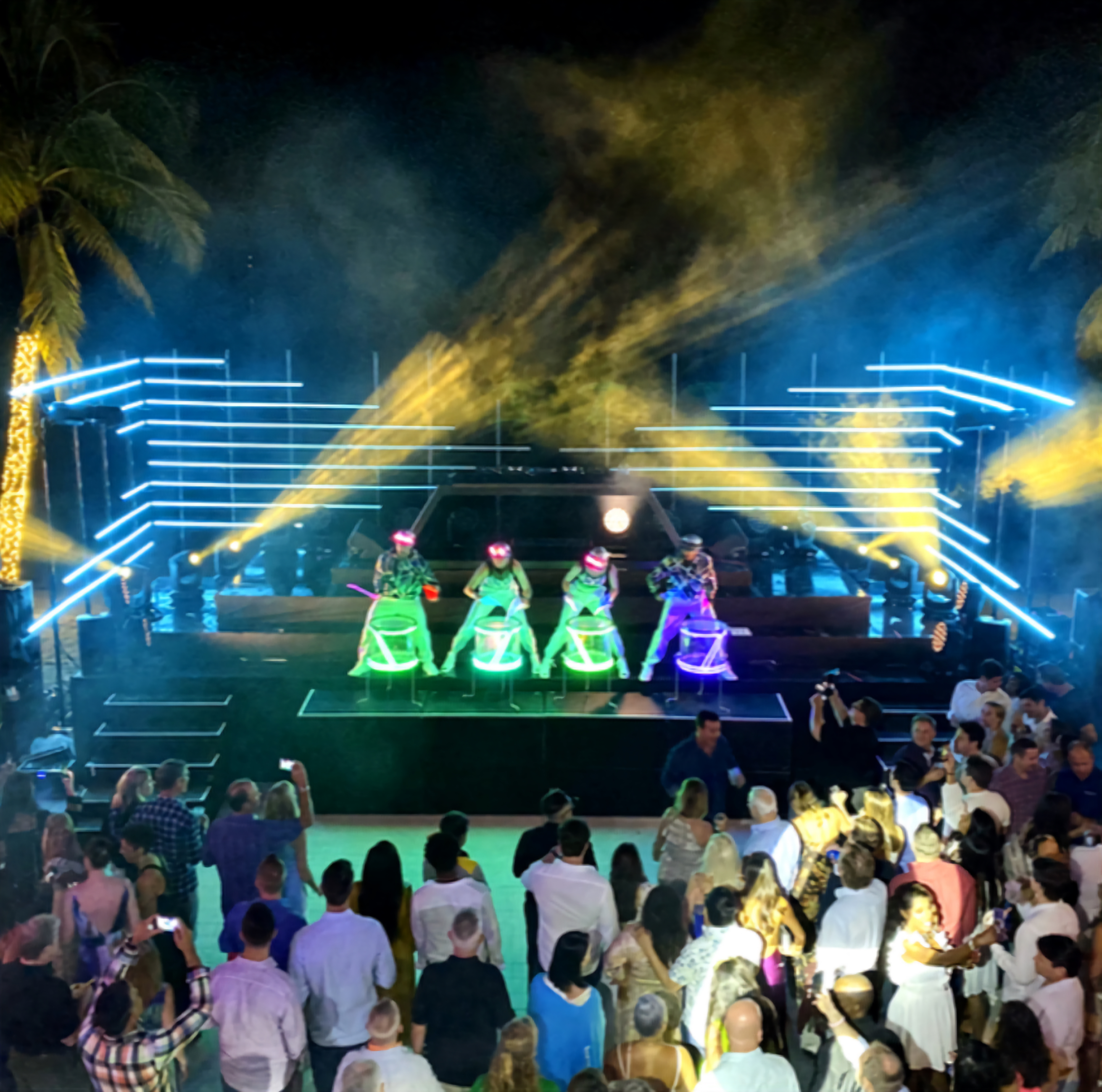 Outdoor nighttime LED drum show with a large crowd and light beams